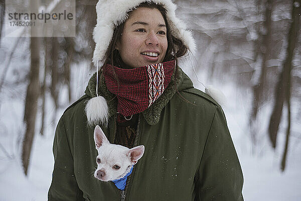 Androgyne asiatische Frau mit niedlichem Chihuahua in ihrer Jacke im Schnee