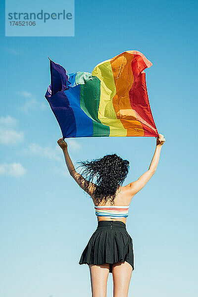 Frau auf dem Rücken mit offenen Armen  die eine LGBT-Flagge schwenkt