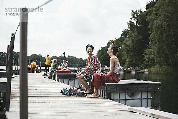 Gemischte Rassenfreunde sitzen lachend auf dem Pier am See in Polen