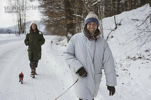 Glückliche Frauen gehen lächelnd im Winter in Tschechien mit Hunden auf einer weißen Schneestraße spazieren