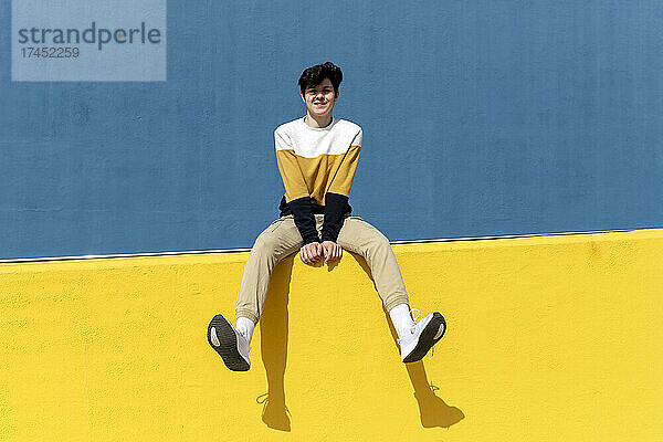Selbstbewusster Mann blickt in die Kamera  während er auf einer gelben Stützmauer sitzt