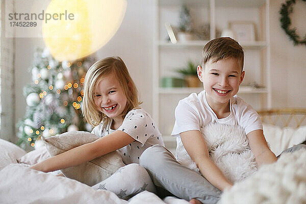 Kinder sitzen auf dem Bett und schauen lächelnd in die Kamera.