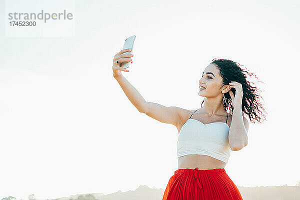 Junge Frau macht ein Selfie mit ihrem Handy und trägt ein weißes Oberteil