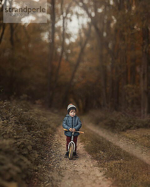 Kleiner Junge in blauer Jacke und Hut auf Pushbike steht auf dem Land