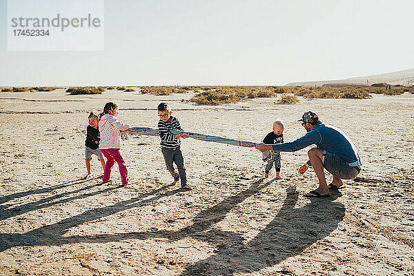 Geschwister und Eltern spielen bei Sonnenuntergang am Strand auf den Kanarischen Inseln