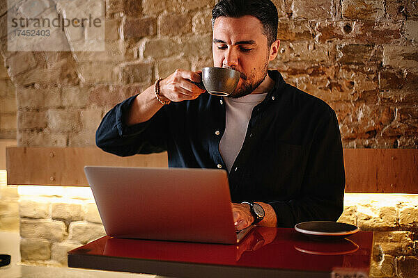 Geschäftsmann trinkt Kaffee  während er im Café einen Laptop-Computer benutzt