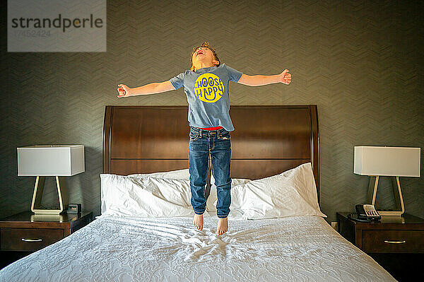 Fröhlicher Junge springt auf einem Hotelbett hoch in die Luft