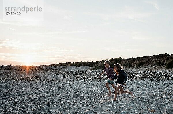 Bruder und Schwester laufen bei Sonnenuntergang gemeinsam am Strand