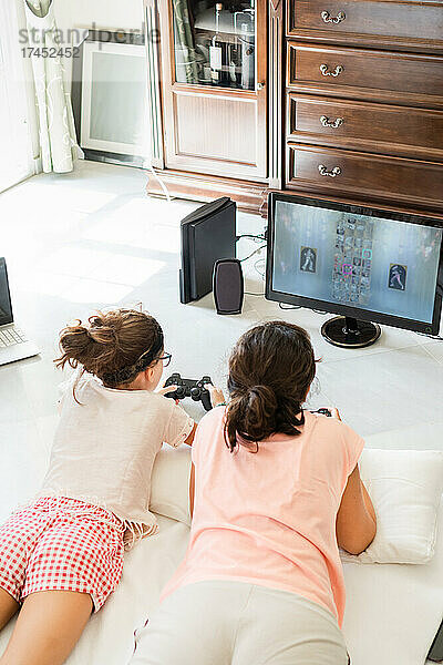 Mutter und Tochter liegen auf dem Boden und spielen zu Hause gemeinsam ein Videospiel