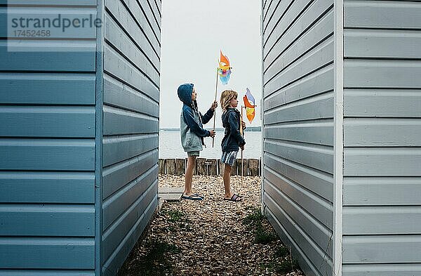 Kinder spielen mit Windmühlen am Strand neben Strandhütten