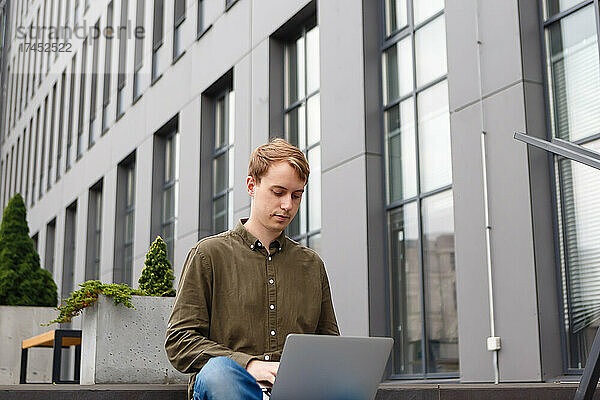 Mann arbeitet am Laptop und sitzt auf der Treppe des Business Centers
