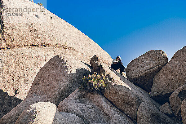 Teenager sitzt allein auf einem felsigen Berg in der Wüste.