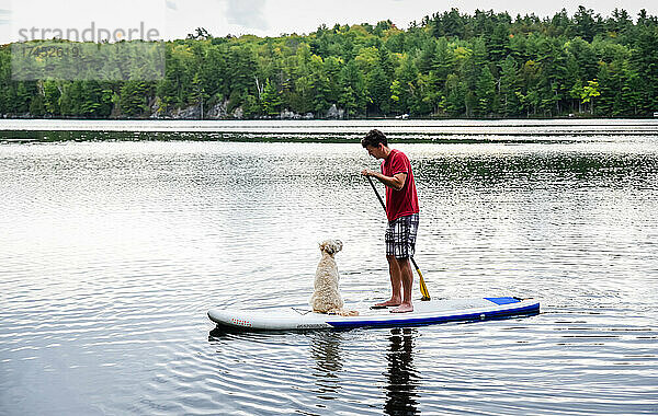 Mann paddelt mit seinem Hund auf einem See auf einem Stand-Up-Paddleboard-SUP.