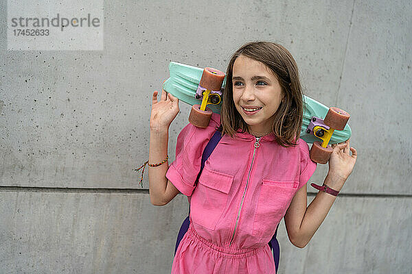 Lächelndes Teenager-Mädchen hält ein Skateboard vor einer Betonwand