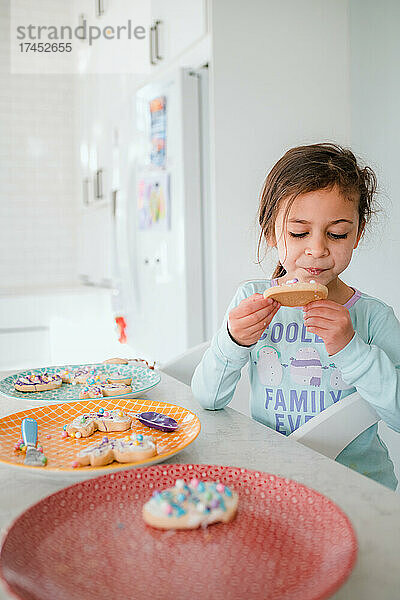Kleines Mädchen dekoriert und isst Osterplätzchen