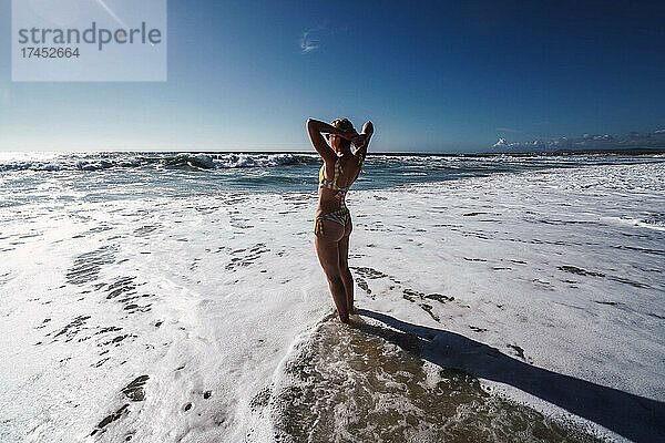 Frau im Badeanzug am Meeresufer mit Wellen mit Schaum am Strand