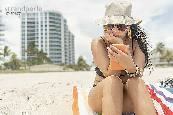 Mädchen am Strand  das ihre sozialen Netzwerke auf ihrem Handy überprüft