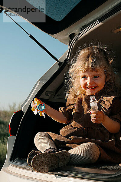 Süßes Mädchen mit Hut  3 Jahre alt  bläst Seifenblasen aus dem Auto