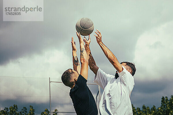 Zwei Freunde springen in die Luft  während sie gegen einen Basketball kämpfen