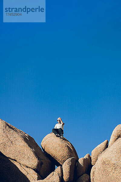 Teenager sitzt auf einem großen Felsen in der Wüste.