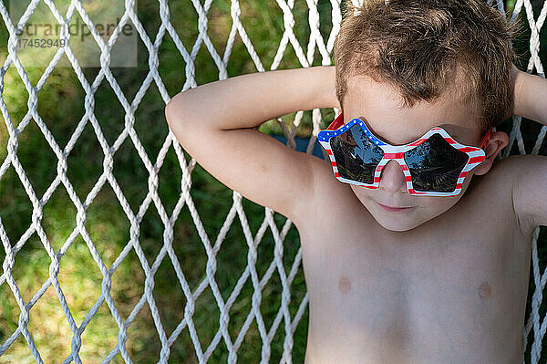 Nahaufnahme eines kleinen Jungen  der sich in einer Hängematte entspannt und eine alberne Sonnenbrille trägt