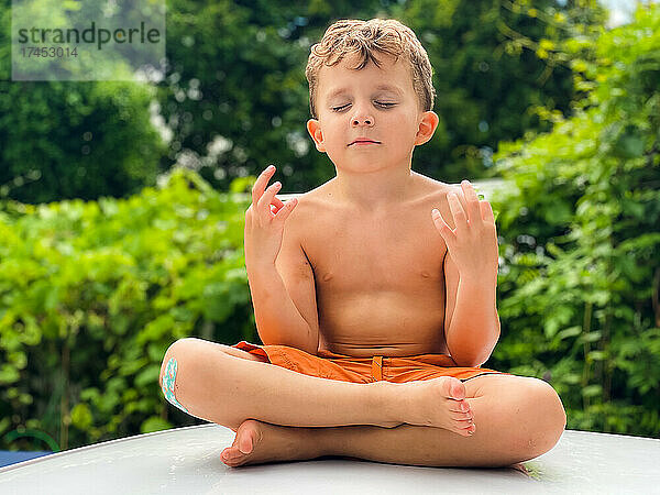 Kleiner Junge meditiert an einem sonnigen Tag im Freien