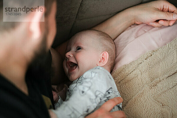 Vater und Baby liegen lächelnd auf dem Bett