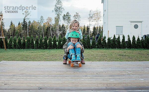 Bruder und Schwester spielen im Herbst auf einem Skateboard im Garten