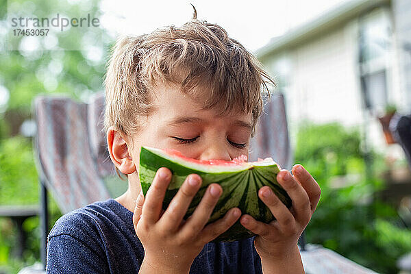 Blonder Junge mit unordentlichem Haar  der mit geschlossenen Augen Wassermelone isst
