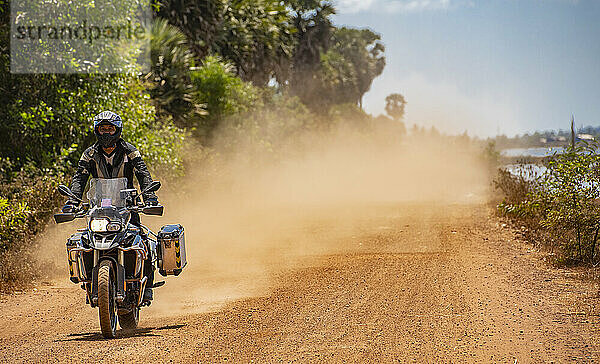 Mann fährt mit seinem Abenteuermotorrad auf staubiger Straße in Kambodscha