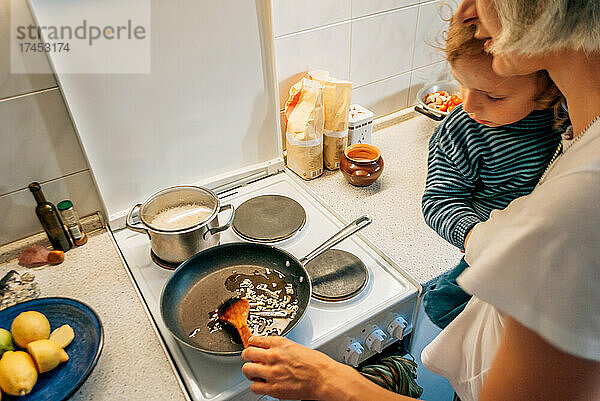 Eine Frau kocht zu Hause mit einem Kind im Arm das Abendessen