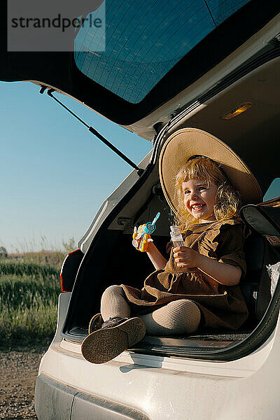 Süßes Mädchen mit Hut  3 Jahre alt  bläst Seifenblasen aus dem Auto