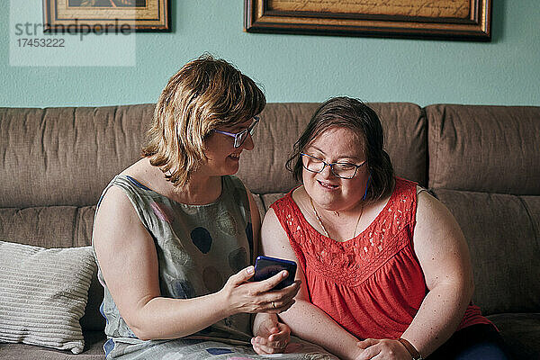 Eine erwachsene Frau und ihre Schwester mit Down-Syndrom schauen zu Hause auf ein Telefon