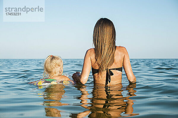 Junge Frau und Kind mit dem Rücken zum Meer