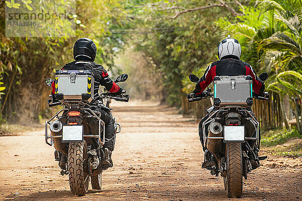 Zwei Männer fahren mit ihrem Abenteuermotorrad auf einer unbefestigten Straße in Kambodscha