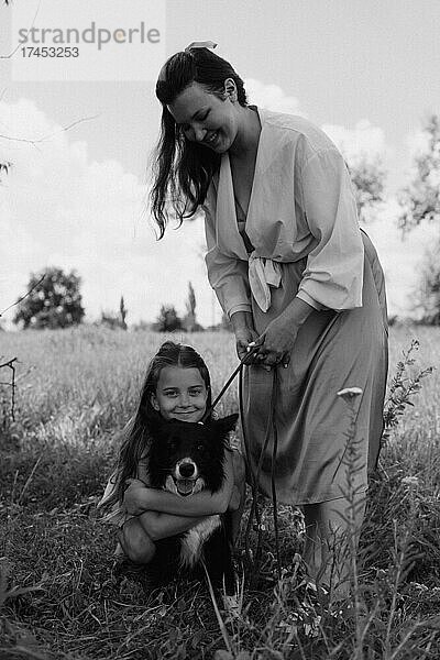 Glückliche Mutter und Mädchen mit Hund im Freien. Haustierpflegekonzept.