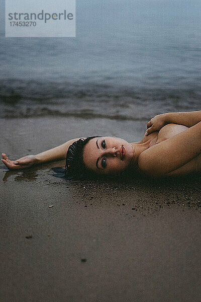 Nackte Frau liegt im Sand