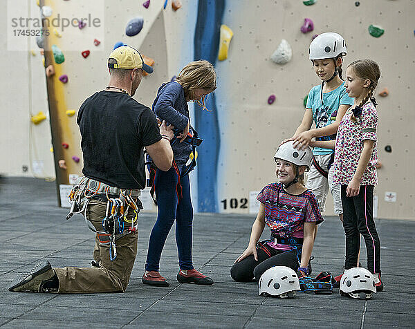 Klettertrainer hilft Mädchen beim Anlegen des Klettergurts