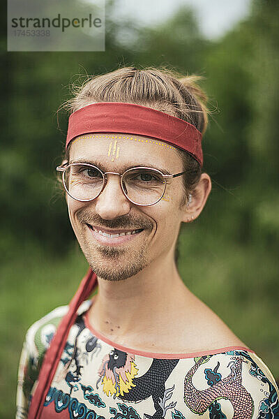 Glücklicher Mann beim Festival mit Brille  Gesichtsbemalung und rotem Kopftuch