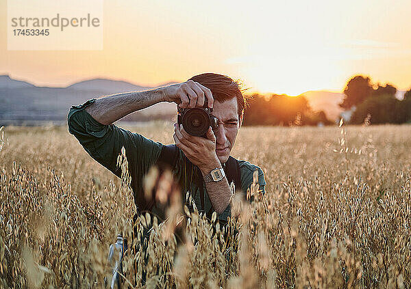 Porträt eines Fotografen  der bei Sonnenuntergang auf einer Wiese in die Kamera blickt
