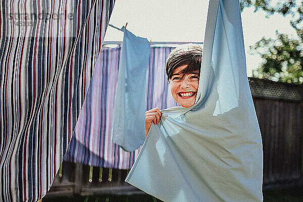 Fröhlicher Junge versteckt sich hinter Kleidung  die draußen an einer Wäscheleine hängt.