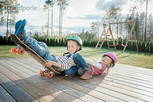 Bruder und Schwester spielen zu Hause gemeinsam auf einem Skateboard und lachen