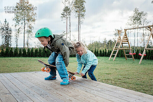 Bruder und Schwester spielen zu Hause im Garten gemeinsam auf einem Skateboard