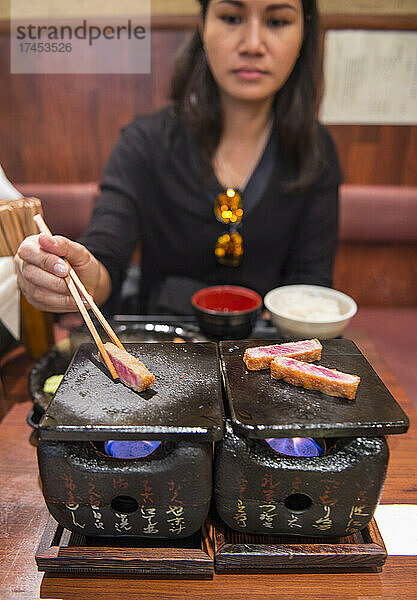 Frau kocht Rindfleisch-Katsu auf einem traditionellen japanischen Lehmofen