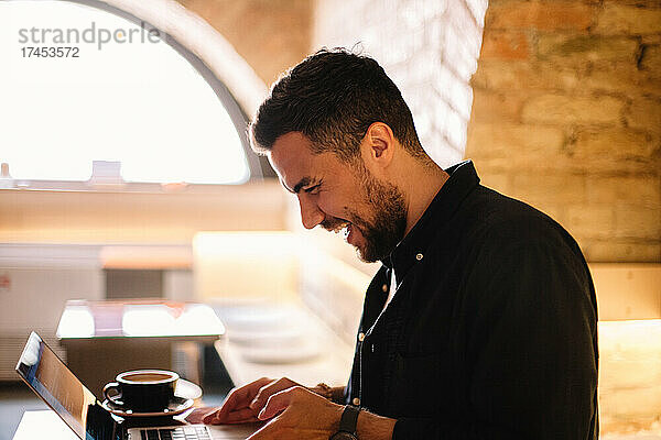 Glücklicher Mann lacht  während er im Café einen Laptop-Computer benutzt