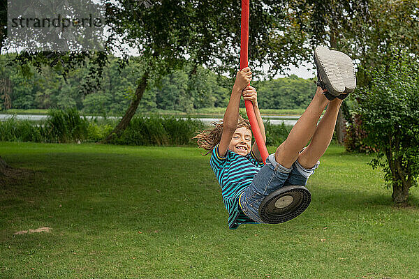 Fröhlicher Junge  der am Wochenendmorgen am Seil auf dem Spielplatz schwingt