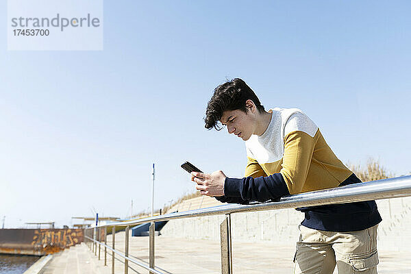 Junger Mann benutzt ein Smartphone und schreibt SMS-Nachrichten  lehnt am Geländer