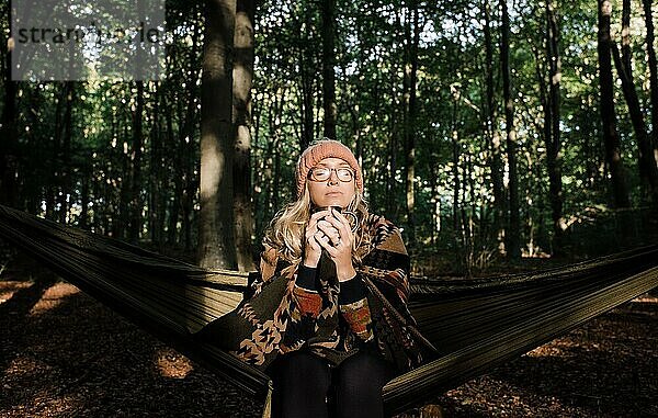 Frau saß auf einer Hängematte im Wald und genoss im Herbst ein heißes Getränk