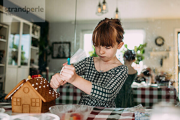 Junges Mädchen konzentriert sich beim Dekorieren des Lebkuchenhauses
