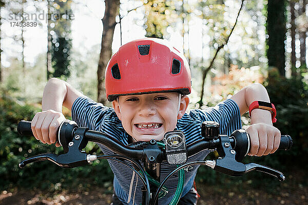 Porträt eines Jungen  der sich lächelnd auf sein Fahrrad im Wald stützt